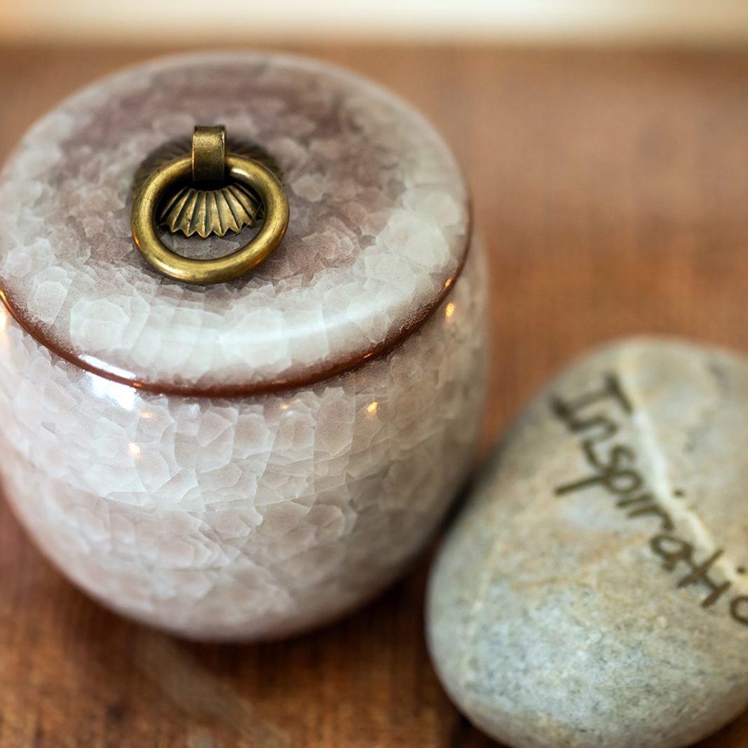 Small ceramic keepsake urn beside a smooth stone engraved with the word Inspiration